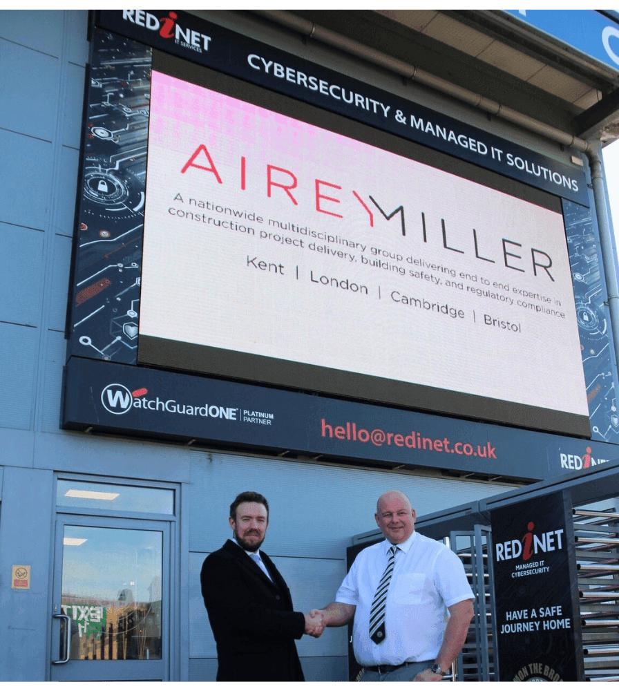 Airey Miller exec shaking hands with Bromley exec in front of large screen